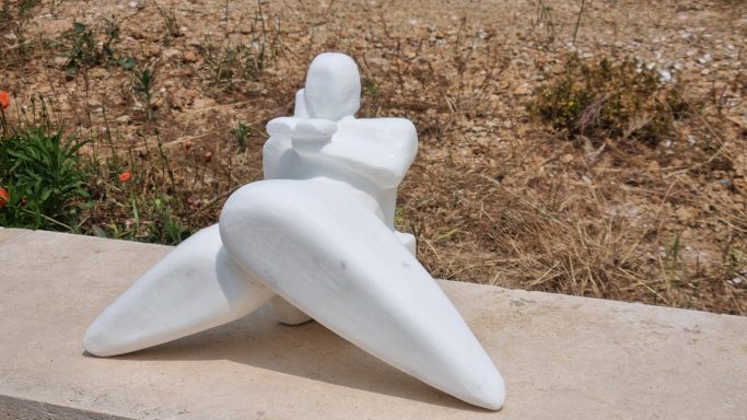 Sculpture blanche d'une figure abstraite, assise avec les jambes croisées.